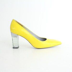 May include: A pair of yellow high-heeled pumps with a clear block heel.