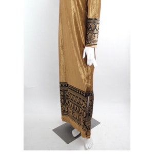 May include: A long, gold velvet dress with black and gold embroidery on the sleeves and hem. The dress has a simple, elegant design and is perfect for a special occasion.