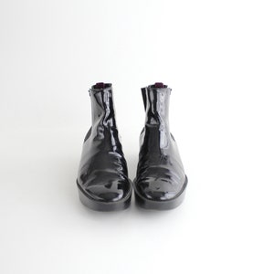 May include: A pair of black patent leather ankle boots with elastic side panels.