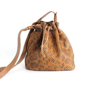 Può includere: Una borsa a secchiello in pelle marrone con motivo a pelle di serpente. La borsa ha una tracolla lunga e una chiusura a coulisse.