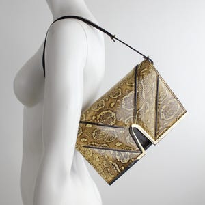 Könnte beinhalten: Eine goldene und braune Schlangenleder-Clutch mit schwarzem Riemen und goldenen Akzenten.