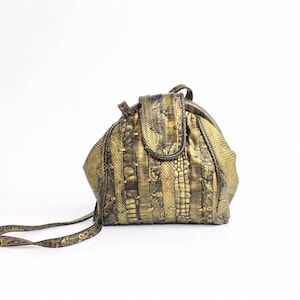 Op de afbeelding: Een ronde schoudertas in goudkleur met een slangenhuidpatroon. De tas heeft een klep sluiting en een lange band.