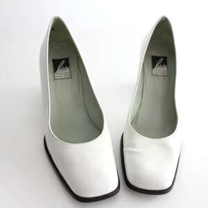 Puede incluir: Par de zapatos de tac&oacute;n de cuero blanco con punta cuadrada y ribete negro. Los zapatos tienen una etiqueta en el interior que dice "Liz Claiborne New York".
