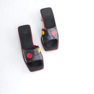 May include: Pair of black leather slide sandals with a square toe and a small heel. The straps are decorated with red, yellow, and blue polka dots. The soles and inner edges are red.