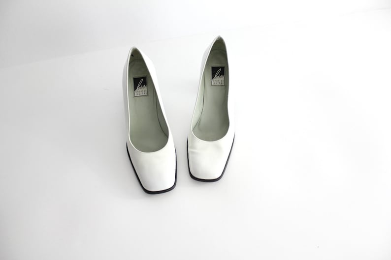 Puede incluir: Un par de zapatos de sal&oacute;n de cuero blanco con puntera cuadrada y tac&oacute;n bajo. Los zapatos tienen una etiqueta negra en el interior que dice "Liz Claiborne New York".