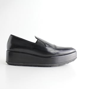 May include: Black leather platform loafers with a pointed toe and a thick platform sole.