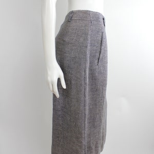 Puede incluir: Una falda gris y blanca a rayas con una silueta recta. La falda es de largo hasta la rodilla y tiene un diseño sencillo.