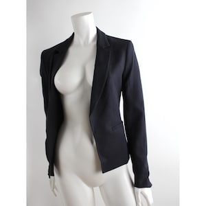 May include: A dark blue blazer with a single button closure and a notched lapel. The blazer has long sleeves and a fitted silhouette.