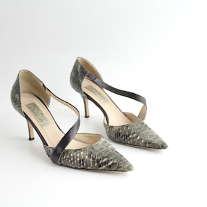 Peut inclure: Une paire de escarpins à talons en peau de serpent gris et noir avec un design de bride croisée. Les chaussures ont une pointe pointue et un talon aiguille.