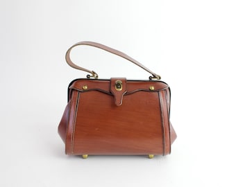 May include: A brown leather handbag with a top handle and a brass clasp. The bag has a vintage style and is decorated with brass studs.