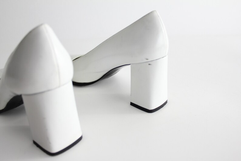 Puede incluir: Un par de zapatos de tac&oacute;n blanco con tac&oacute;n de bloque. Los zapatos est&aacute;n hechos de un material liso y brillante.