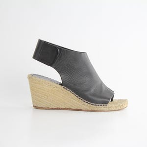 May include: Black leather wedge sandals with a closed toe and an ankle strap. The wedge is made of a natural material, possibly jute or rope.