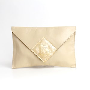 Può includere: Una pochette in pelle beige con una toppa dorata a forma di diamante sul davanti.