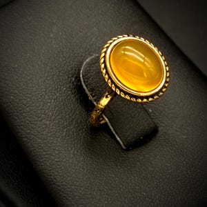 Op de afbeelding: Een gouden ring met een grote, ronde, gele edelsteen gezet in een gouden zetting.