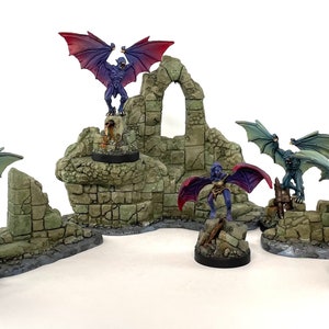 May include: Five miniature figures of winged creatures, painted in shades of blue and purple, stand on various ruined stone structures. The figures are posed in dynamic stances, with wings spread and claws extended. The stone structures are painted in shades of gray and green, with details of crumbling walls and overgrown vegetation.