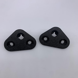 May include: Two black plastic triangular shaped pieces with three holes each. The pieces are designed to be used as mounting brackets.