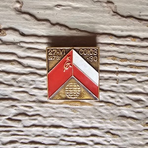May include: A gold-colored metal pin with a red, white, and gold design. The pin features a red triangle with a white star and a hammer and sickle symbol. The text "27-VI 1978г" and "СОЮЗ -30" is printed on the pin.