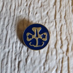 May include: A blue and gold Girl Scout pin with a three-leaf clover design and two stars.