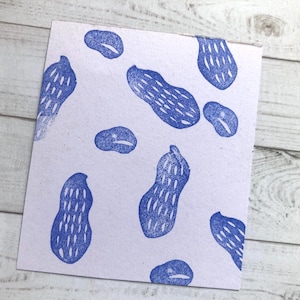 Puede incluir: Una tarjeta blanca con un patrón de cacahuetes azules. Los cacahuetes están impresos en un estilo simple y en bloque.