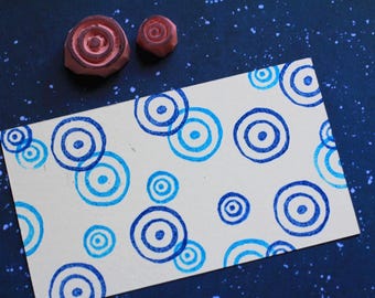 May include: A white card with a blue and white concentric circle pattern printed on it. Two red rubber stamps are visible in the background.