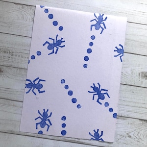 Puede incluir: Papel blanco con un patrón de hormigas azules y puntos. Las hormigas caminan en línea, siguiendo los puntos.