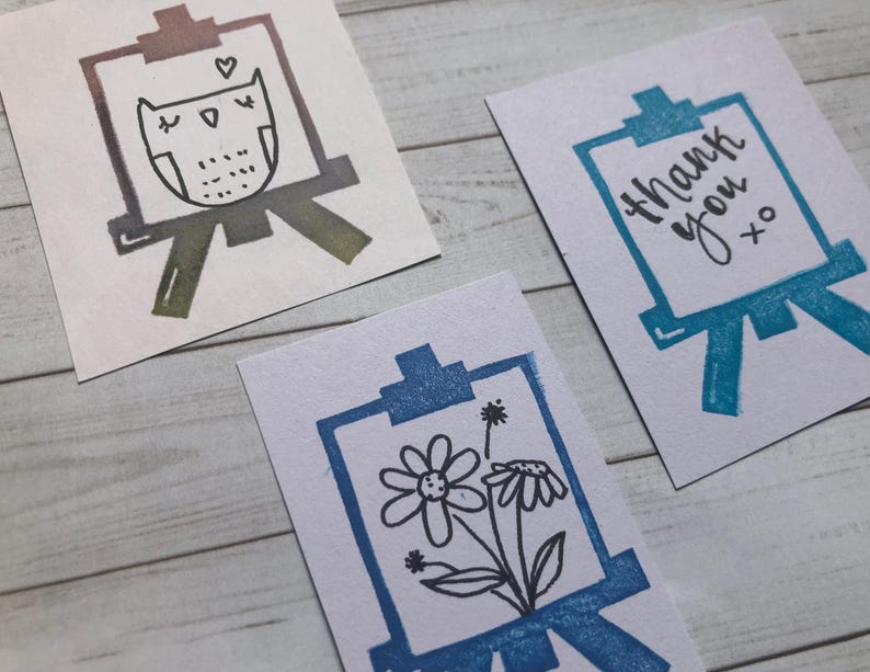 May include: Three small, white cards with illustrations of easels. One card features an owl design, another says "thank you xo", and the third has a floral design. The easel illustrations are in shades of blue, green, and purple.