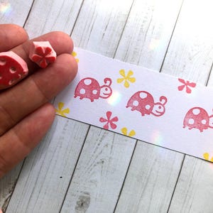 May include: A set of five red and white ladybug rubber stamps with yellow flower designs on a white background. The stamps are arranged in a row on the white surface.