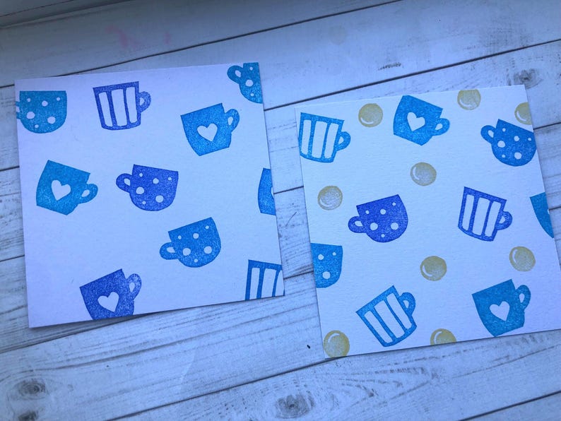 May include: Two white cards with a repeating pattern of blue teacups. The teacups have different designs, including polka dots, stripes, and heart shapes. Some cards also have small yellow circles scattered across the surface.