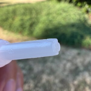 May include: Close-up of a white plastic nozzle with a small hole on the side. The nozzle is designed for dispensing liquids.