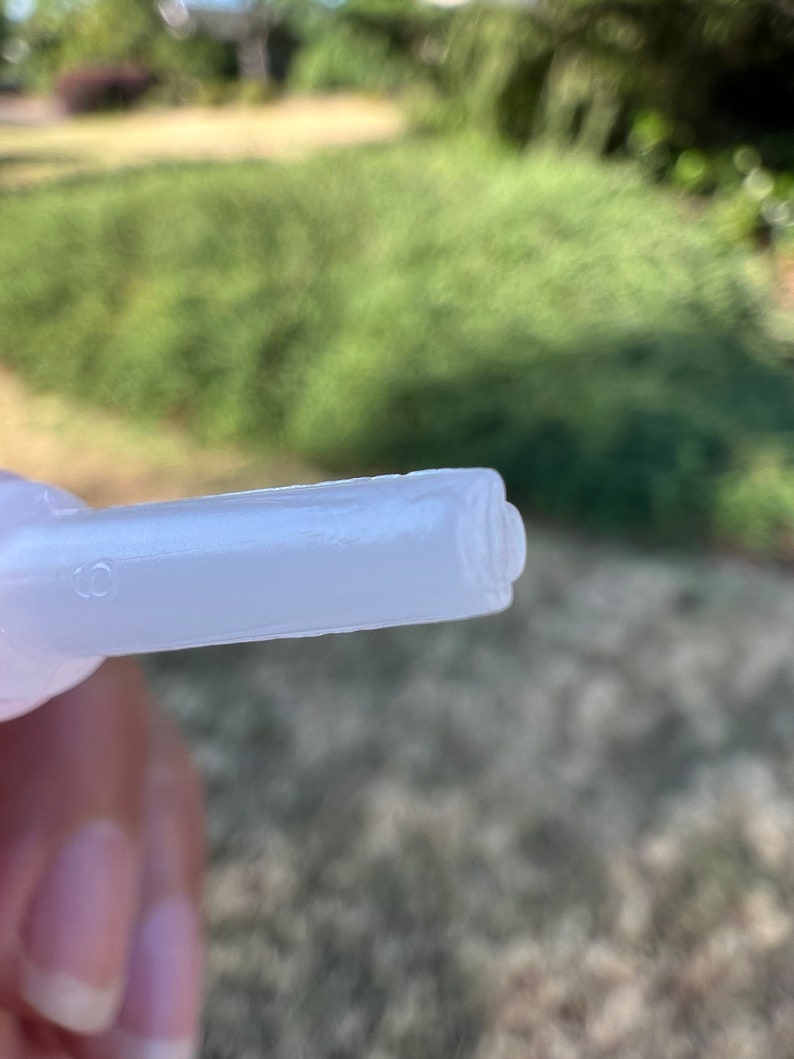 May include: Close-up of a white plastic nozzle with a small hole on the side. The nozzle is designed for dispensing liquids.
