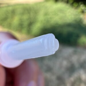 May include: Close-up of a clear plastic applicator tip with a small opening at the end.