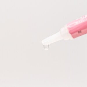 May include: A close-up of a pink and white tube with a clear tip dispensing a drop of liquid.