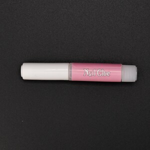 May include: A white and pink nail glue tube with the words "Nail Glue" printed on the pink section.