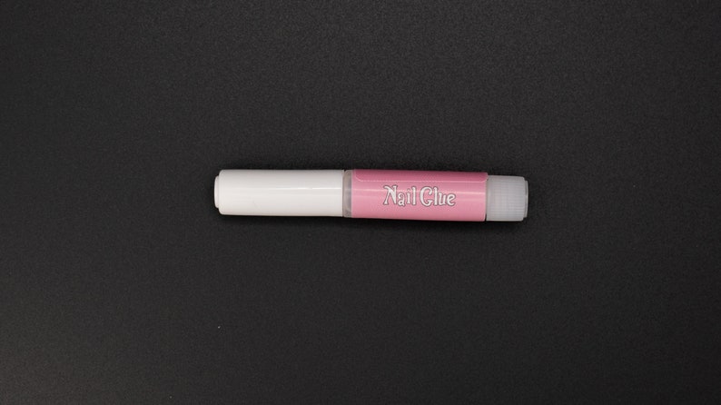 May include: A white and pink nail glue tube with the words "Nail Glue" printed on the pink section.