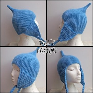 Op de afbeelding: Een lichtblauwe, handgehaakte muts met een puntige bovenkant en oorflappen. De muts wordt getoond op een mannequinhoofd. De tekst "Talli's Designs" is zichtbaar in de afbeelding.