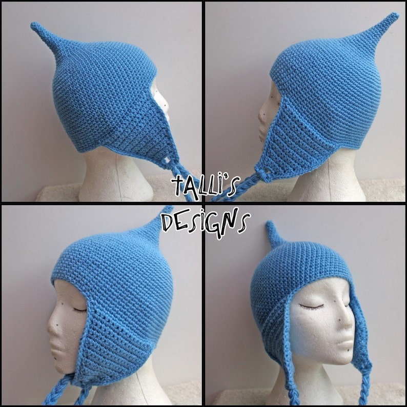 Op de afbeelding: Een lichtblauwe, handgehaakte muts met een puntige bovenkant en oorflappen. De muts wordt getoond op een mannequinhoofd. De tekst "Talli's Designs" is zichtbaar in de afbeelding.