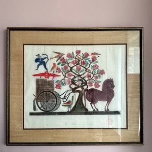 May include: A framed print of a colorful folk art style illustration depicting a horse-drawn carriage with a figure holding a bow and arrow, birds, and a tree with red flowers.