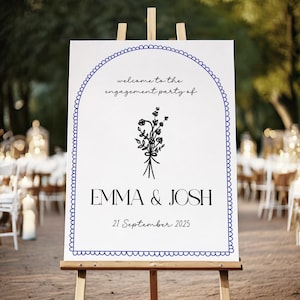 Op de afbeelding: Een wit bord op een houten ezel, dat gasten verwelkomt op een verlovingsfeest. Het bord heeft een blauwe geschulpte rand en een boogontwerp. Tekst bevat "welcome to the engagement party of", de namen "EMMA & JOSH" en de datum "21 September 2025".
