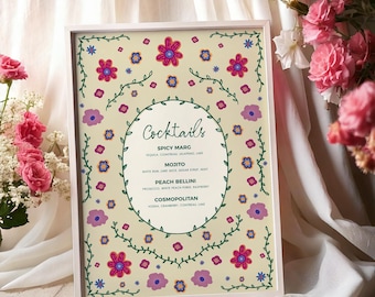 Puede incluir: Un letrero enmarcado con un fondo crema, con un diseño floral y la palabra "Cocktails". El letrero enumera los nombres de los cócteles: Spicy Marg, Mojito, Peach Bellini y Cosmopolitan. Flores rosas y moradas y enredaderas verdes decoran el borde.