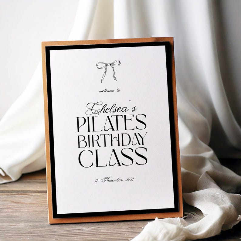 May include: A framed sign with a white background and black text that reads "Chelsea's Pilates Birthday Class" with the date "11 November 2021". The frame is black with a gold border.