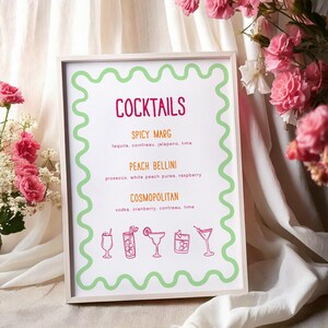 May include: A white sign with a green border and the word "Cocktails" in pink lettering. The sign lists four cocktails with their ingredients: Spicy Marg, Peach Bellini, Cosmopolitan, and a fourth cocktail with an illegible name. Each cocktail is illustrated with a small line drawing of a glass.