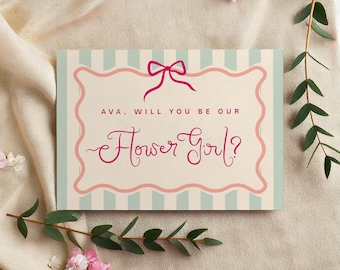 Könnte beinhalten: Rechteckige Karte mit rosa Schleife und dem Text "AVA, WILL YOU BE OUR Flower Girl?" in dekorativer Schrift. Die Karte hat einen hellblau-weiß gestreiften Hintergrund und einen rosa gewellten Rand. Die Karte ist von rosa Blumen und Grün umgeben.