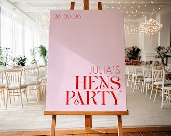 Könnte beinhalten: Ein rosa Schild auf einer Holzstaffelei mit dem Text "Julia's Hens Party" in Rot. Das Datum "23.09.26" ist oben aufgedruckt. Das Schild befindet sich in einem Raum mit weißen Stühlen und Tischen.