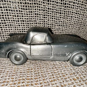 Peut inclure: Une voiture miniature en métal argenté avec un intérieur noir et l'inscription "Chevrolet" sur le côté.