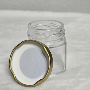 May include: A clear glass jar with a gold lid. The lid has a white liner.