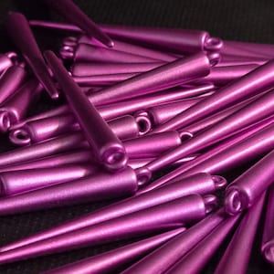May include: A pile of purple metallic cone-shaped beads. The beads have a shiny finish and are arranged in a random pattern.