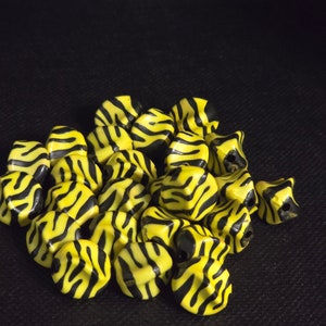 Pode incluir: Um monte de contas de plástico listradas de amarelo e preto. As contas têm a forma de um hexágono arredondado.