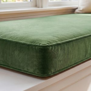 May include: A rectangular bench cushion upholstered in a solid sage green velvet fabric. The cushion features clean, structured edges with piped seams along the perimeter, providing a smooth, uniform surface texture across the top and sides.