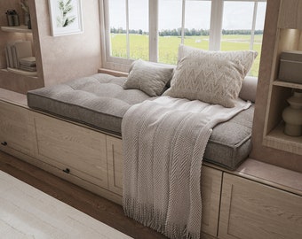 May include: A built-in window seat featuring a tufted gray cushion, a light beige throw blanket with a herringbone pattern and fringe, and two decorative pillows in beige and cream tones, set within a light wood frame with storage drawers.