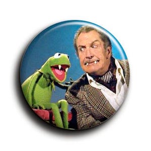 Könnte beinhalten: Ein runder Knopf mit Kermit dem Frosch und einem Mann in einer Tweedjacke. Kermit ist grün mit rotem Mund, und der Mann hat einen Schnurrbart und trägt einen gemusterten Schal. Der Knopf hat einen blauen Hintergrund.